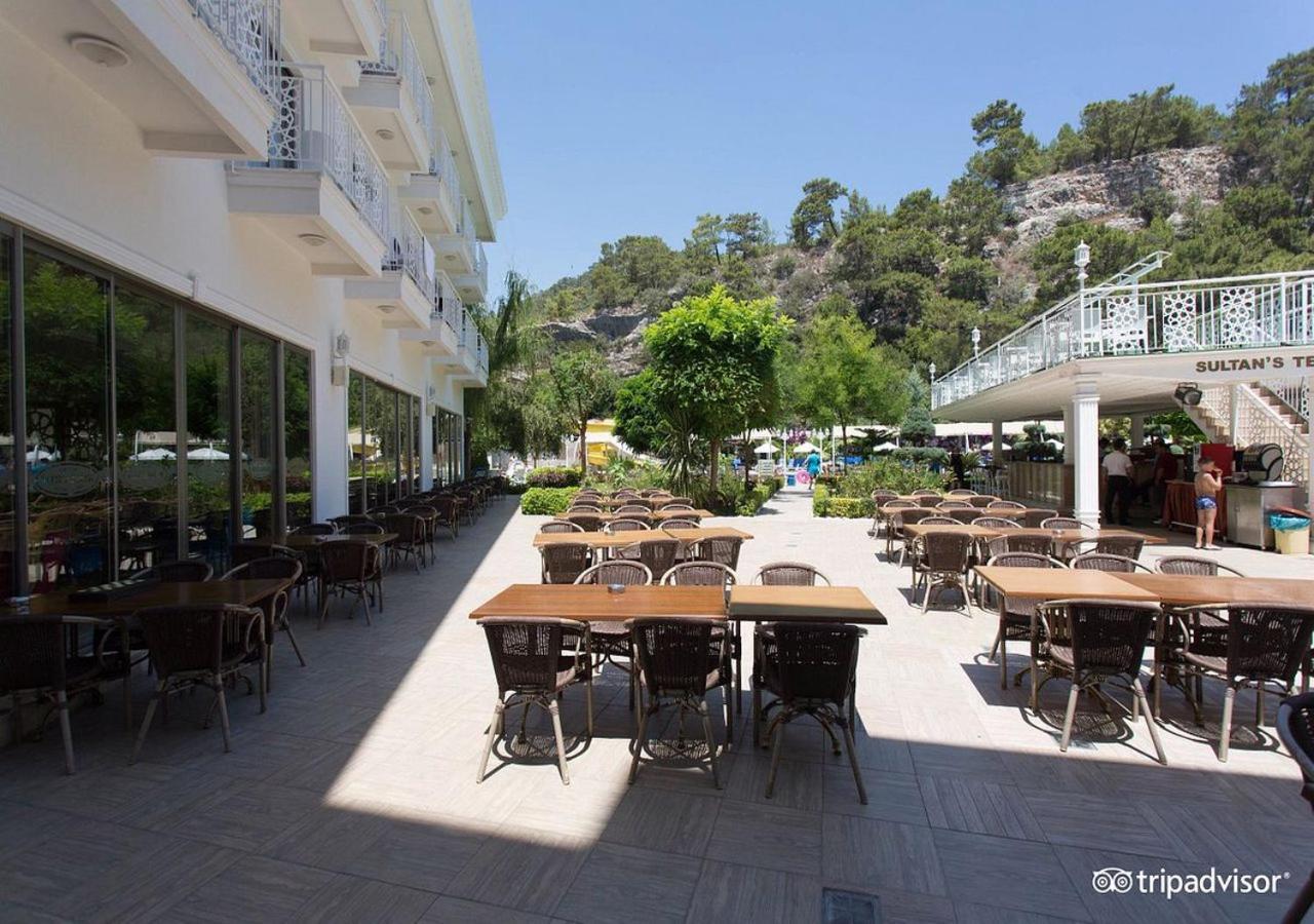 Miramor Hotel & Spa Antalya Exterior photo The photo shows an outdoor dining area, likely at a restaurant or cafe. There are several tables with chairs arranged neatly on the paved ground, and some greenery, such as trees and plants, is visible in the background. The setting appears bright an